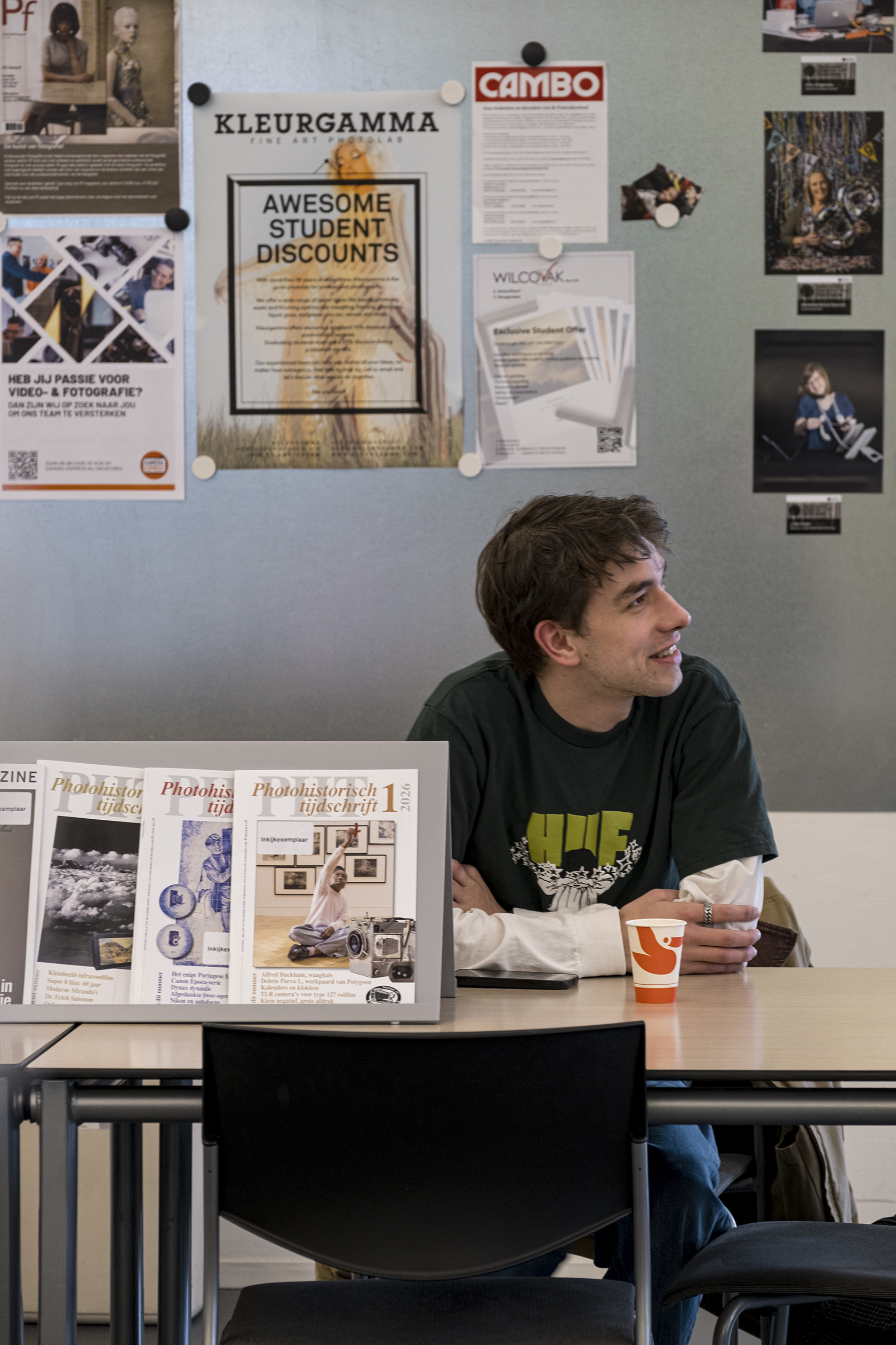 Student kijkt opzij aan tafel met fotografie en posters aan de muur
