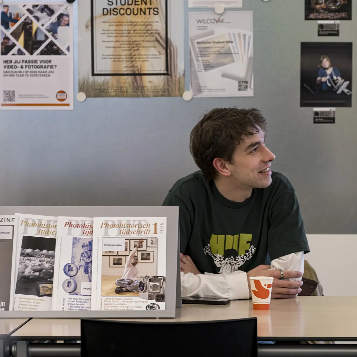 Student kijkt opzij aan tafel met fotografie en posters aan de muur