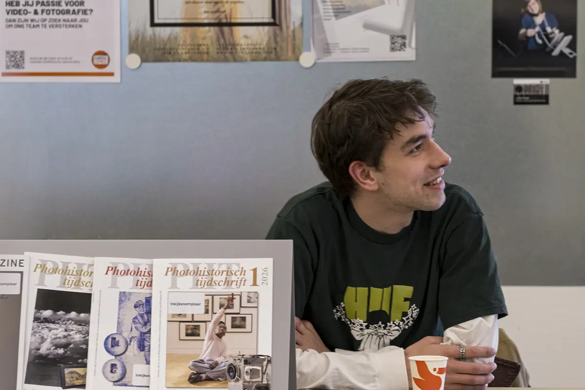 Student kijkt opzij aan tafel met fotografie en posters aan de muur