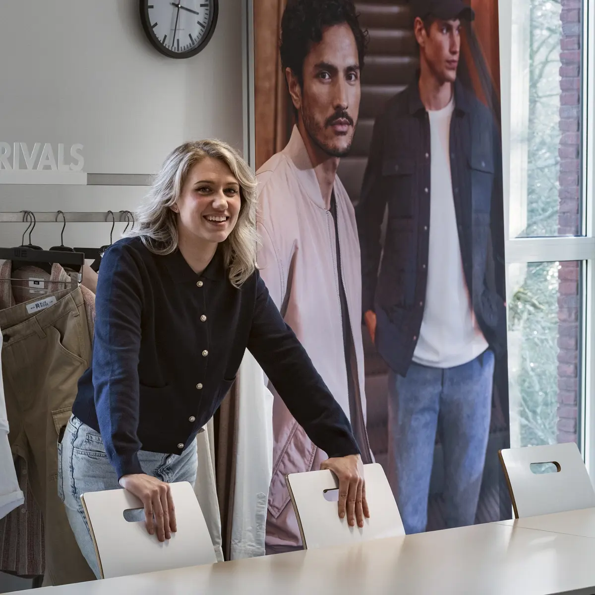 Docent van modeopleiding lokaal met kleding en poster op de achtergrond