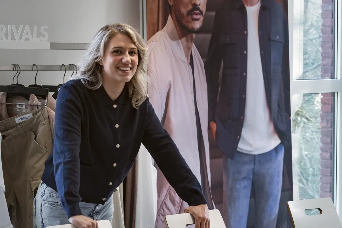 Docent van modeopleiding lokaal met kleding en poster op de achtergrond