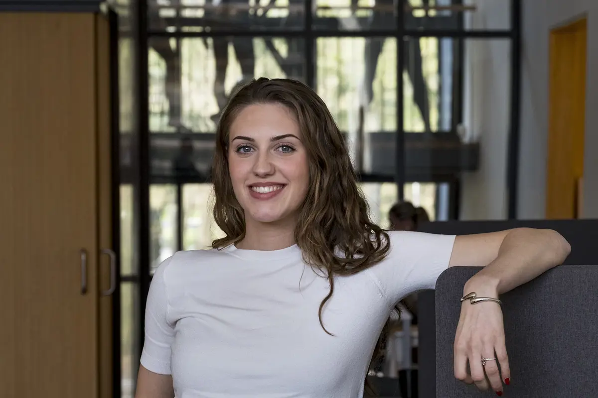 Student staat in een ruimte van een modeopleiding en kijkt in de camera