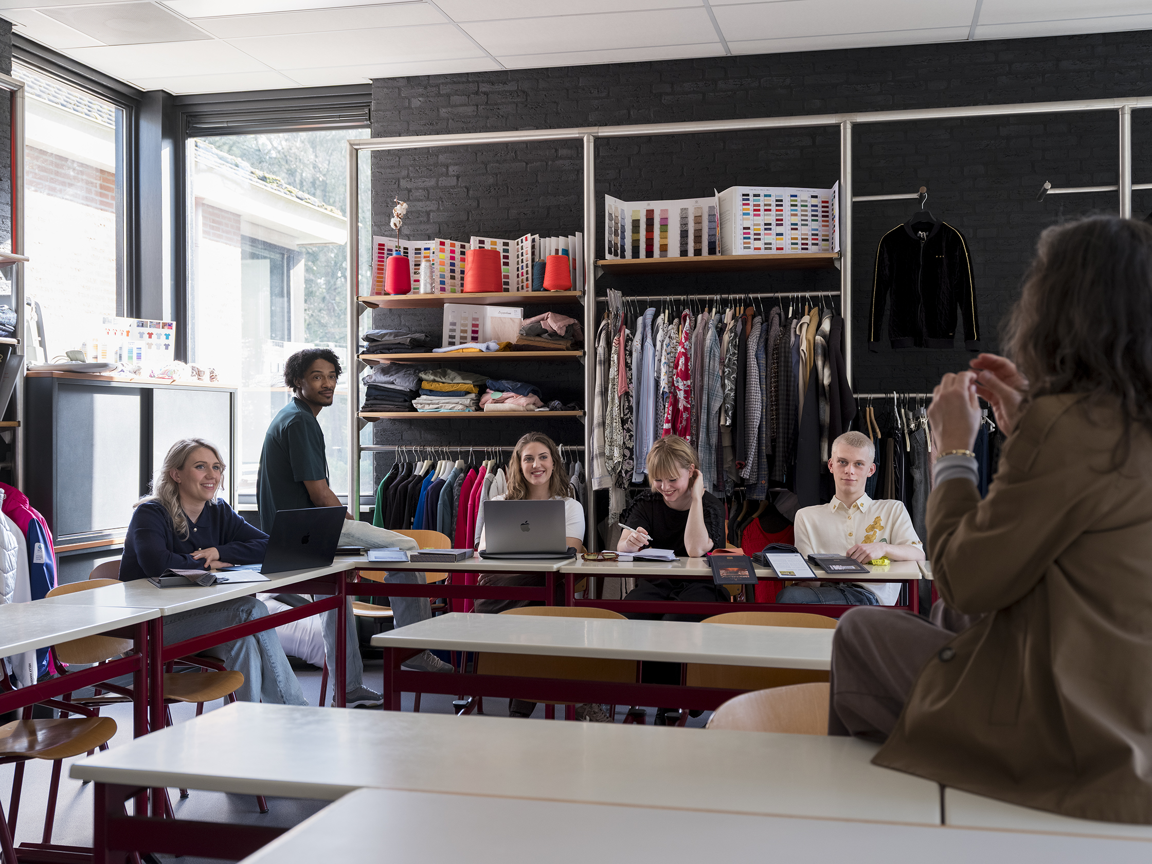 Groep studenten zit in een klaslokaal tijdens een les met docent van een modeopleiding