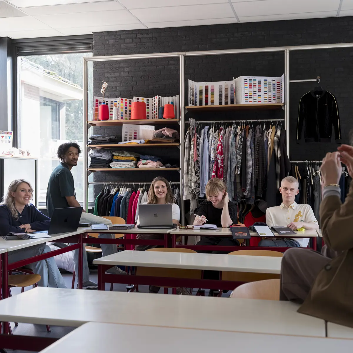 Groep studenten zit in een klaslokaal tijdens een les met docent van een modeopleiding