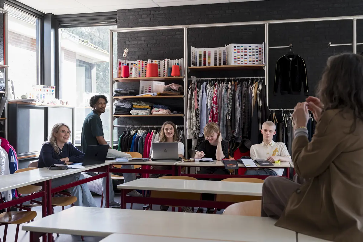 Groep studenten zit in een klaslokaal tijdens een les met docent van een modeopleiding